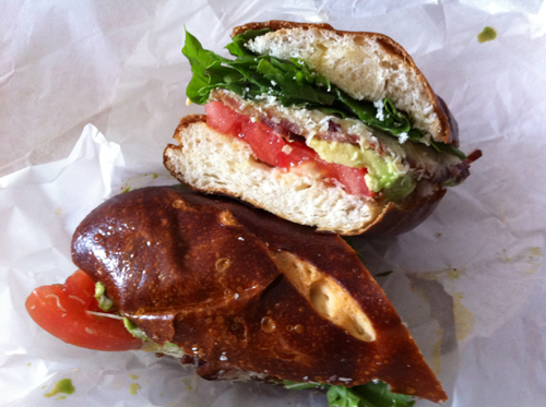 Tomato, arugula, avocado, parmesan, bacon and olive oil on a delicious brown sweet pretzel roll.