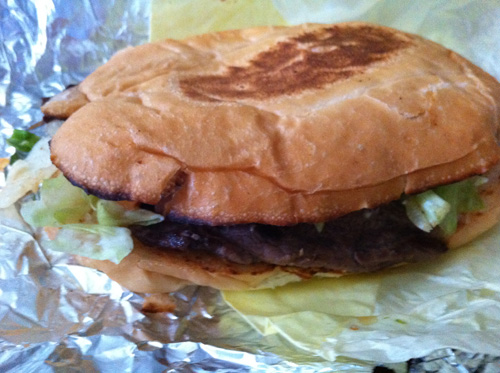 A run-of-the-mill steak sandwich on a flat, oval, slightly-charred roll.